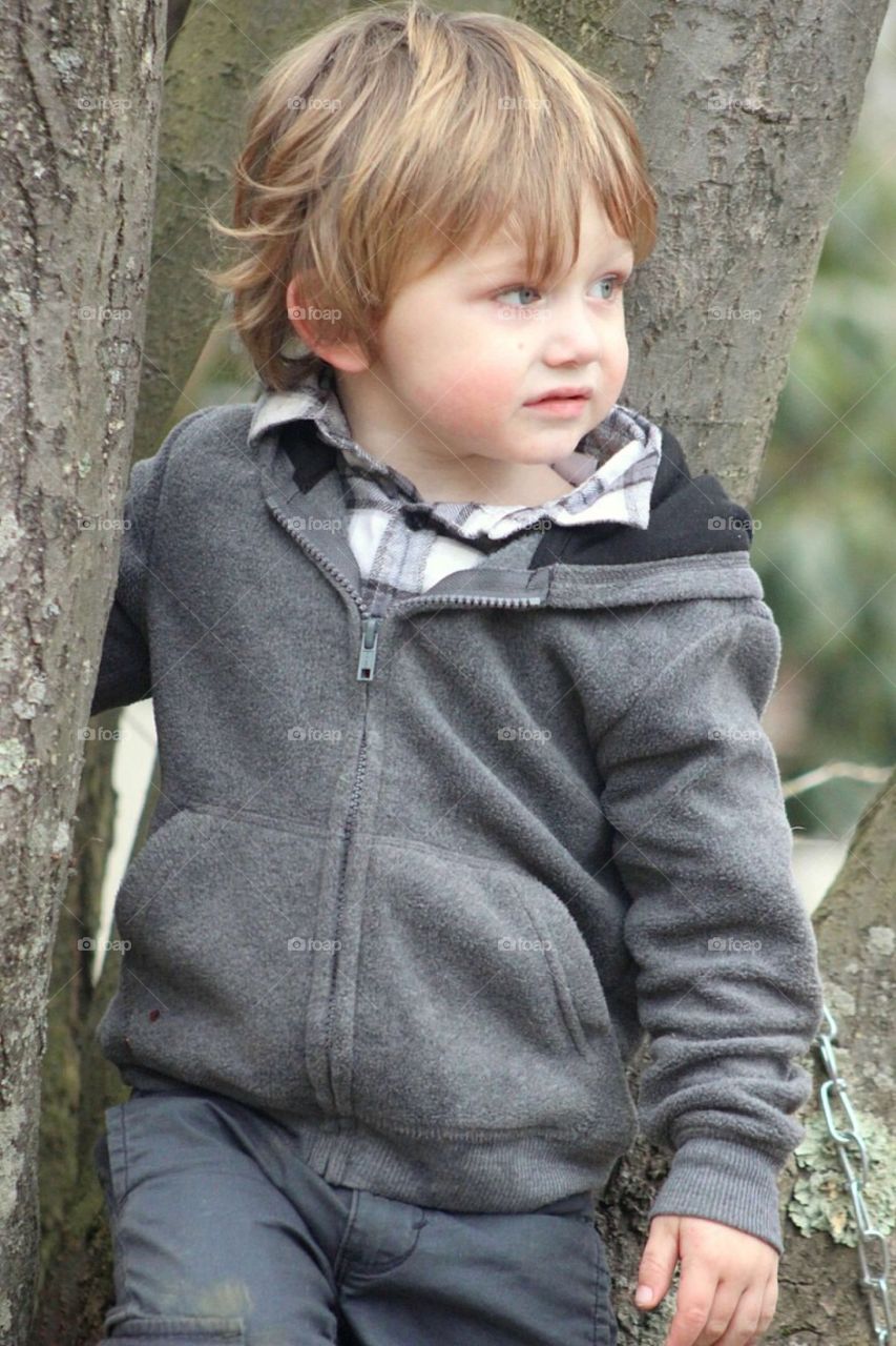 Adorable boy standing near tree trunk
