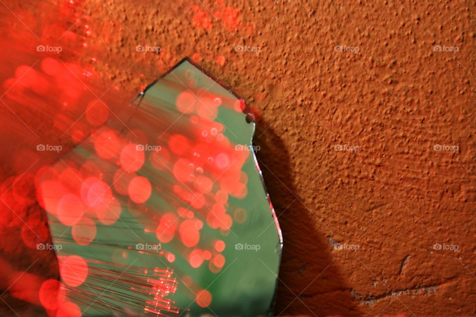 Reflection of red fiber optic lights in broken mirror with green background