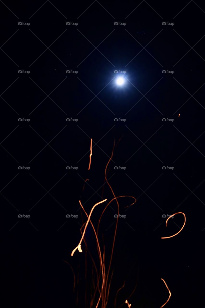 Spark from a fire floating up towards the moon on a clear night.