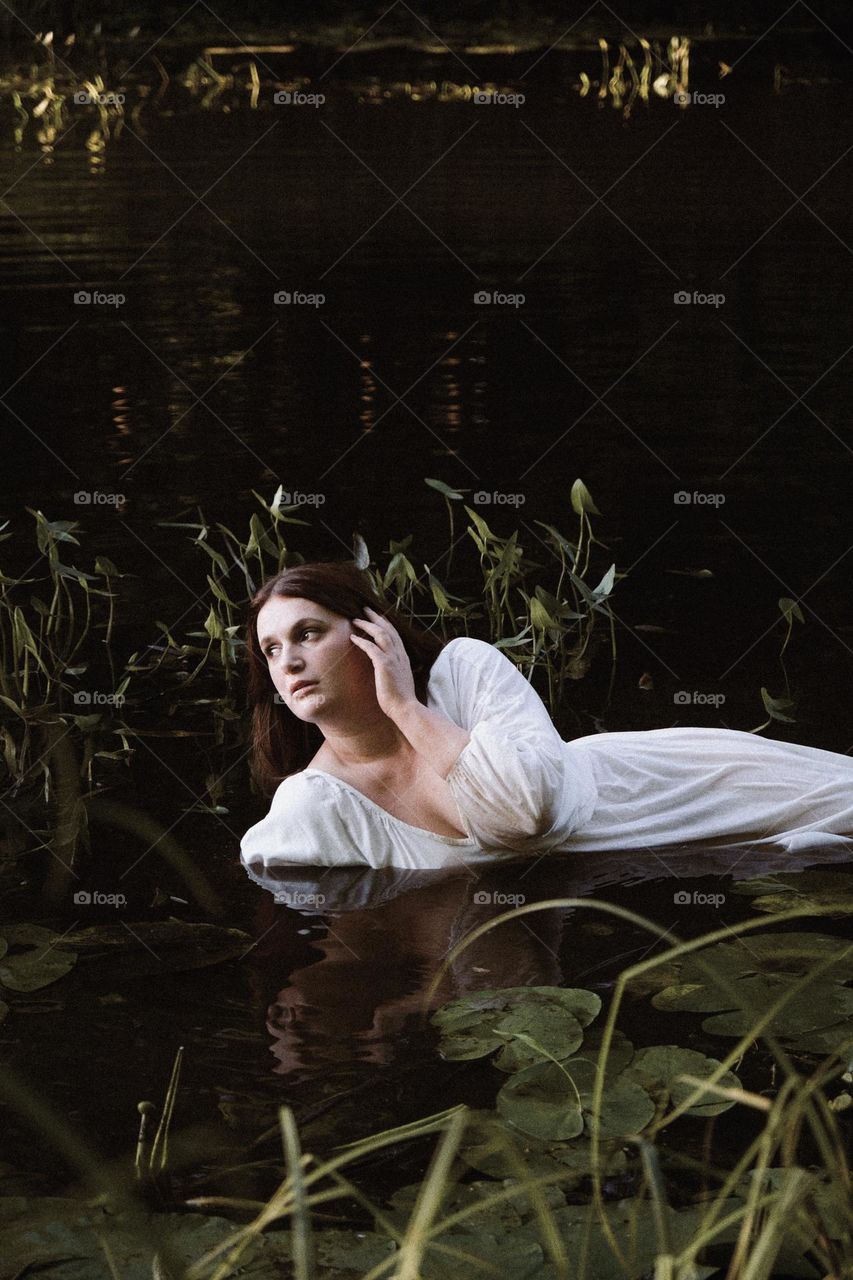 an unusual photo of a light-skinned girl in a river among green water lilies