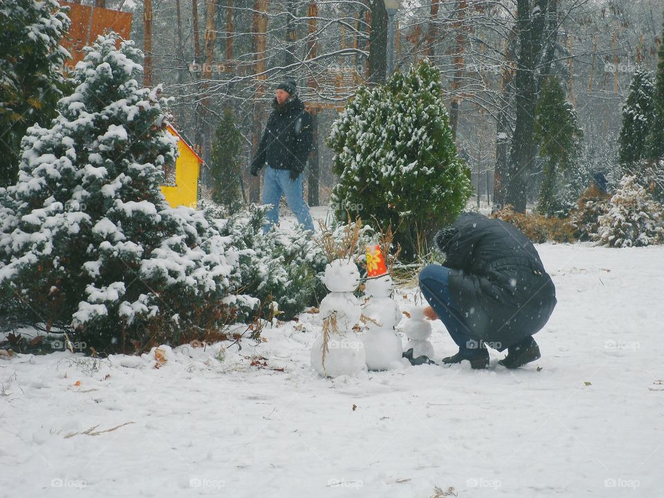 man sculpts a snowman in winter park