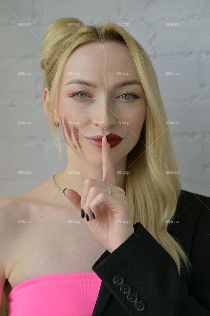 Close-up portrait of a blonde smiling girl with different make-up on half of her face which points to silence on white background