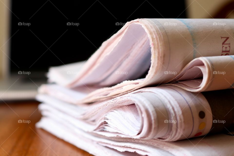 Pile or stack of folded paper newspapers closeup on wood office desk, with dark computer screen background, concept business and finance, reading and education, learning and current events, closeup 