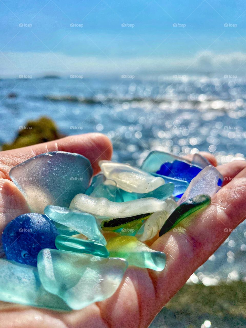 Picking up colorful sea glass in shades of blue on a summer day at the beach, ocean twinkling in the background 