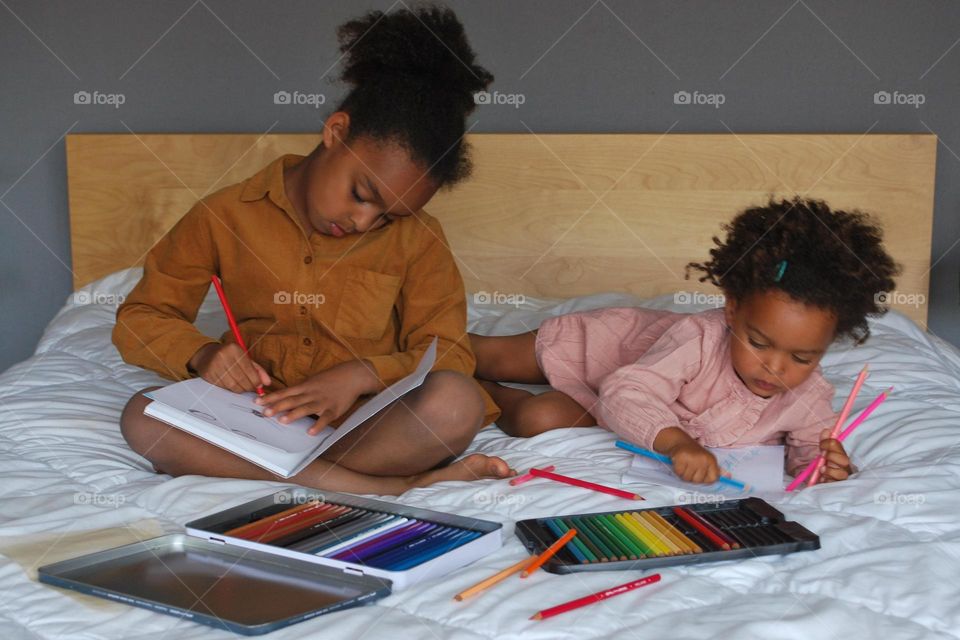 Two little girls of mixed race coloring in bed