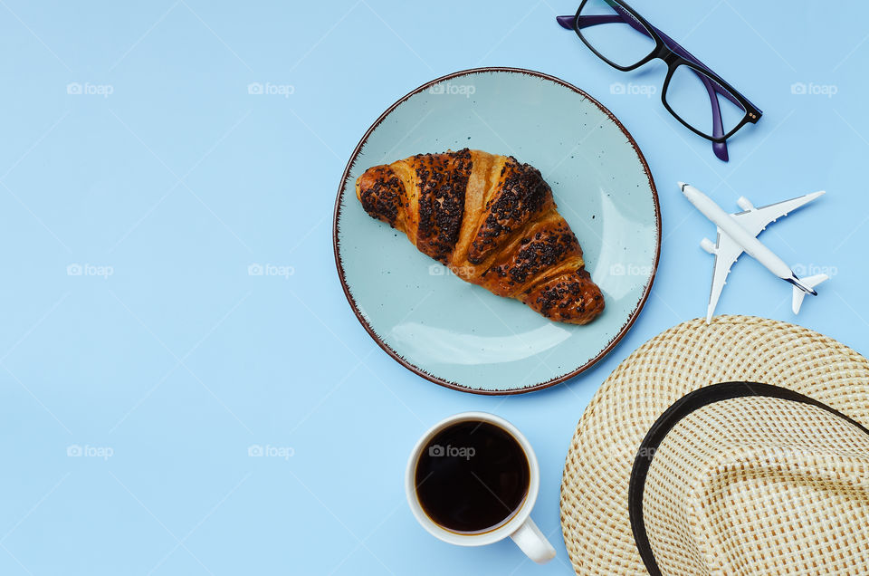 Business working morning with cup of hot coffee, fresh delicious croissant, glasses, hat on blue background close up. Top view, copy space, flat lay, mockup.