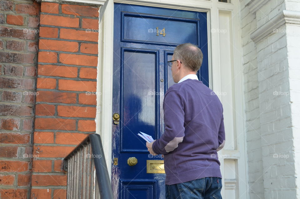 Male canvasser knocking on a blue door and standing outside