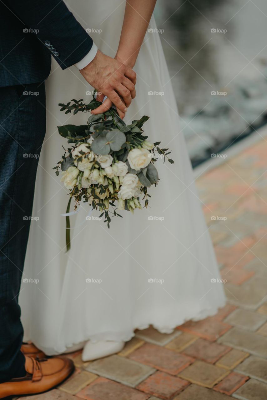 A wedding bouquet of white roses and greenery in the hands of the bride