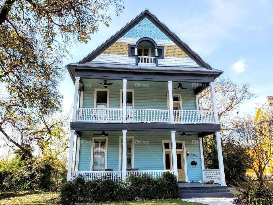 Light blue two story historic home with a second floor balcony and an attic window and balcony.