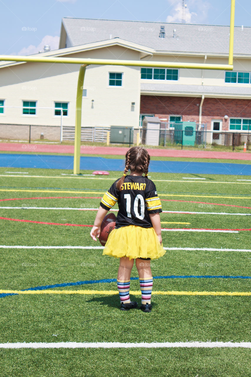 little girl in Pittsburgh Steelers Jersey on a football field staring at goal post
