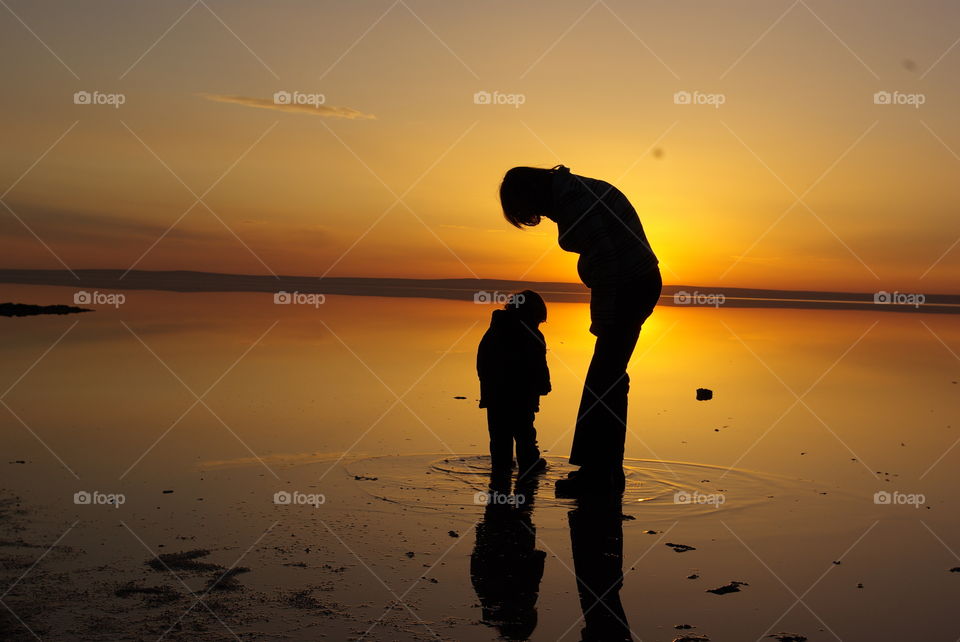 Two people standing in water at sunset