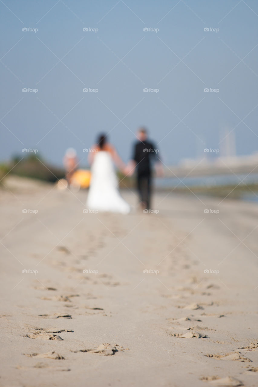 Out of focus newly wed couple walking on the beach in the distance showing their footsteps in  focus