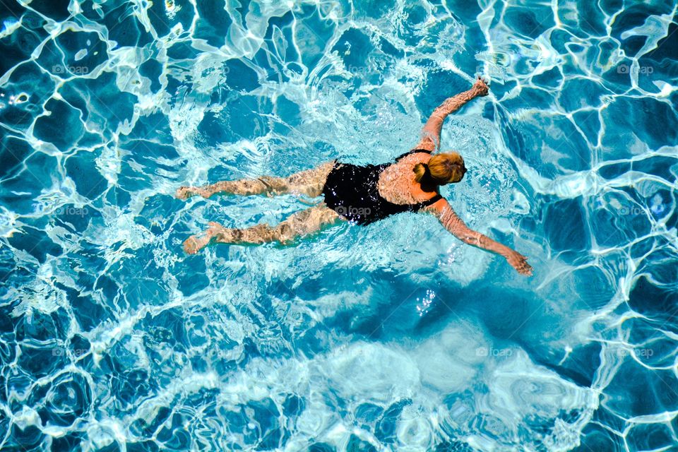 A woman swims in a clear blue swimming pool. 