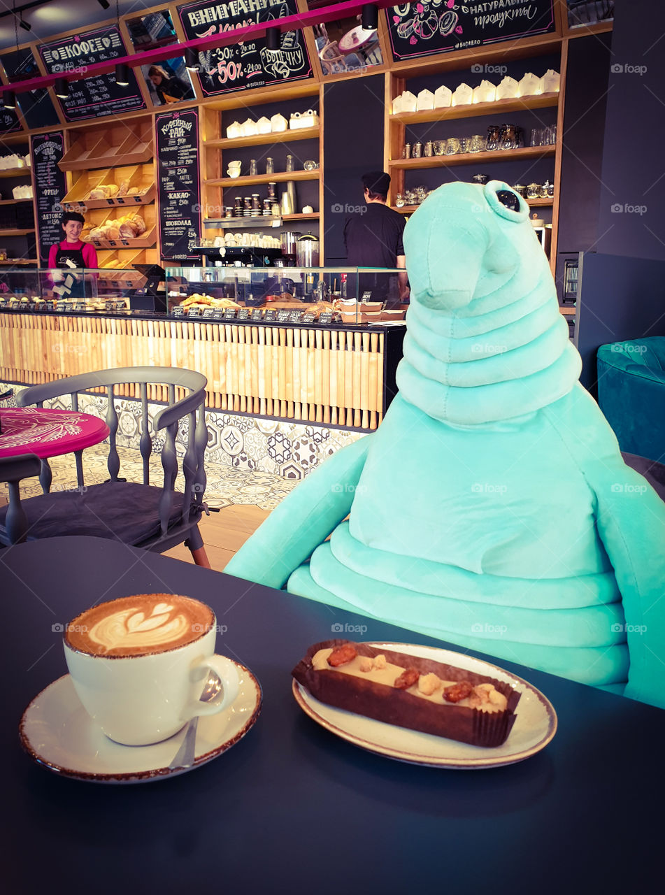 French cafe confectionery in the center of Moscow.  Charming soft toy sitting at the table with a cup of freshly brewed coffee and cake