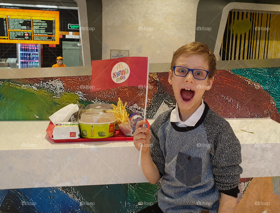 Happy boy in mcdonalds with a tray of food and with a flag in hand.  Fast food