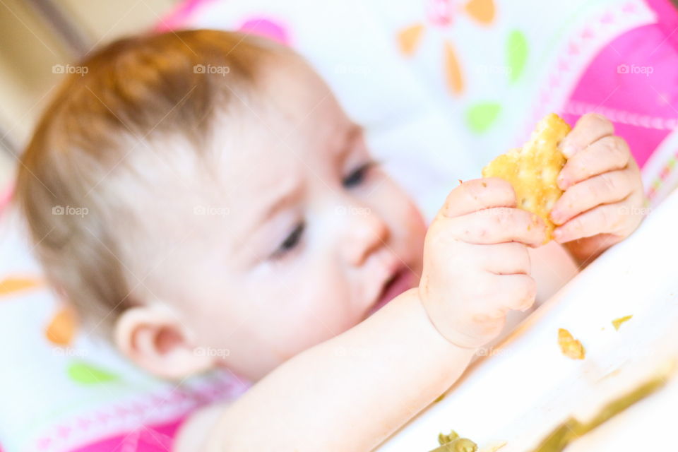 Baby clutching cracker snack sitting in high chair 