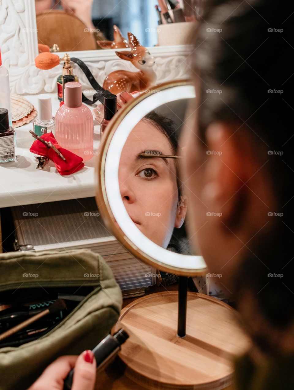 Portrait of young woman doing her make-up in front of circular led illuminated mirror