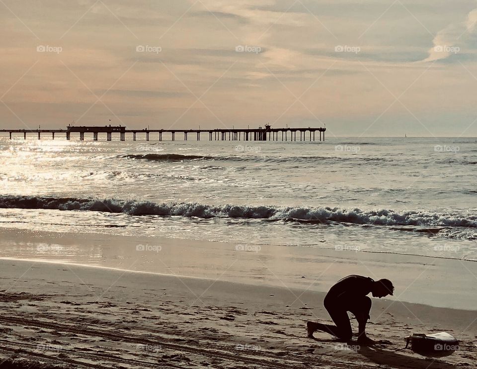 The silhouette of a surfer preparing on an early morning in Ocean Beach, California. Soft sunlight skips off the waves.