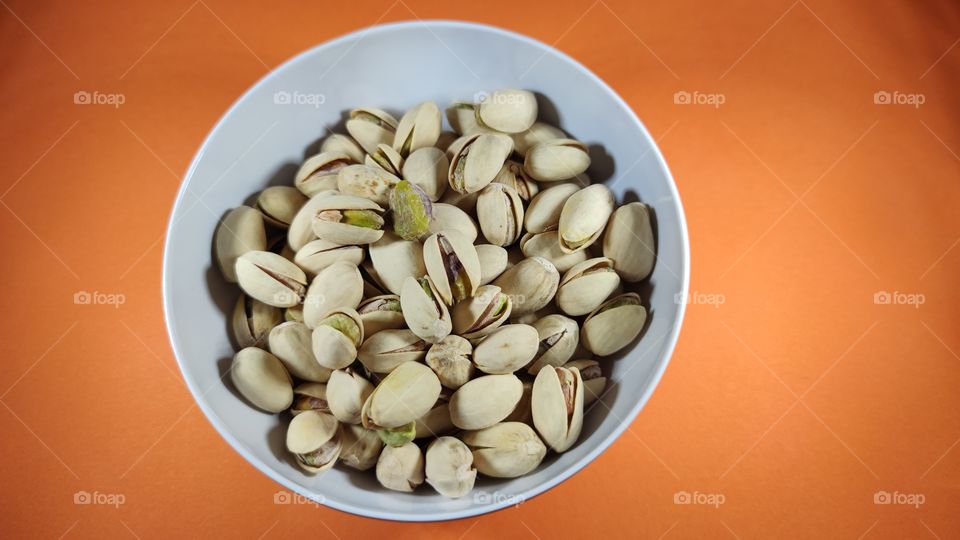 Pistachios in a bowl on an orange background
