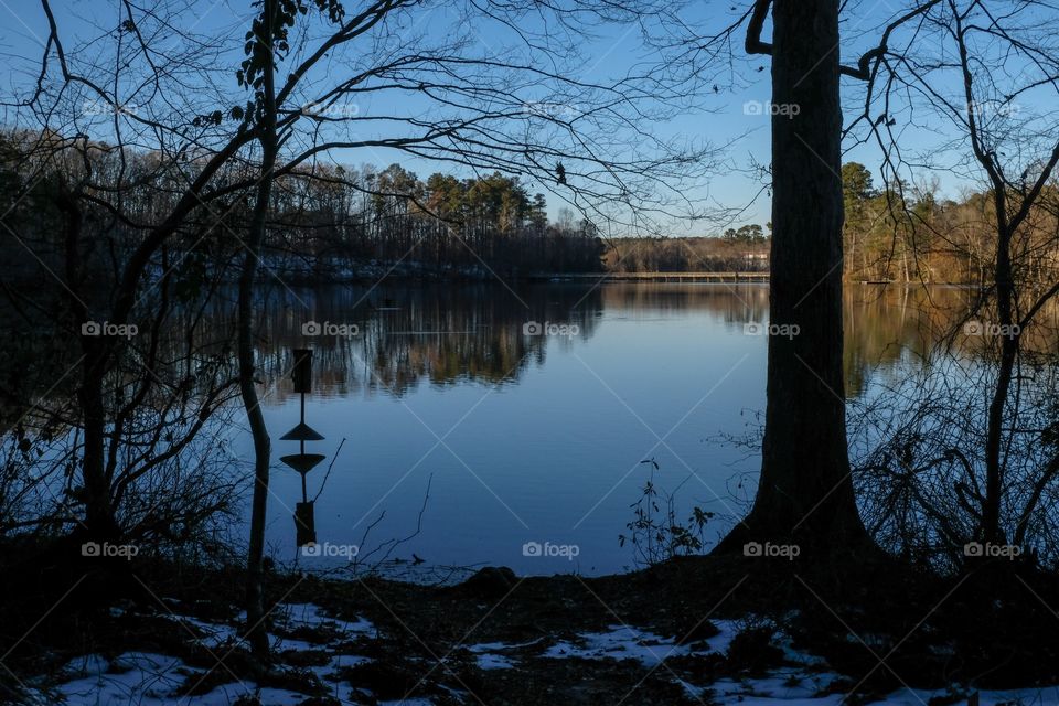 The waning sunshine strikes the opposite shore, with a silhouette and reflection of a wood duck box in the millpond at Yates Mill County Park in Raleigh North Carolina.