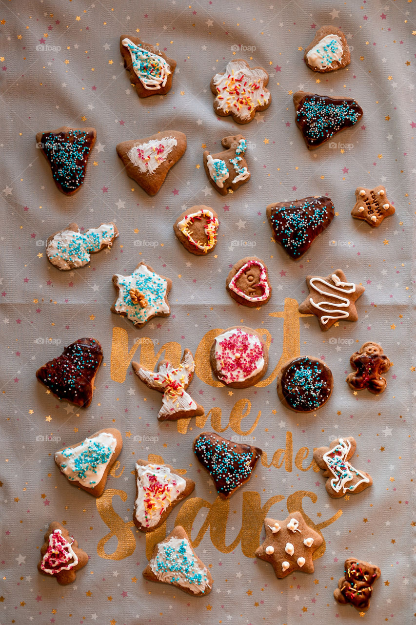 Christmas gingerbread cookies in many shapes decorated with colorful frosting, sprinkle, icing, chocolate coating, toppers, put on plain fabric