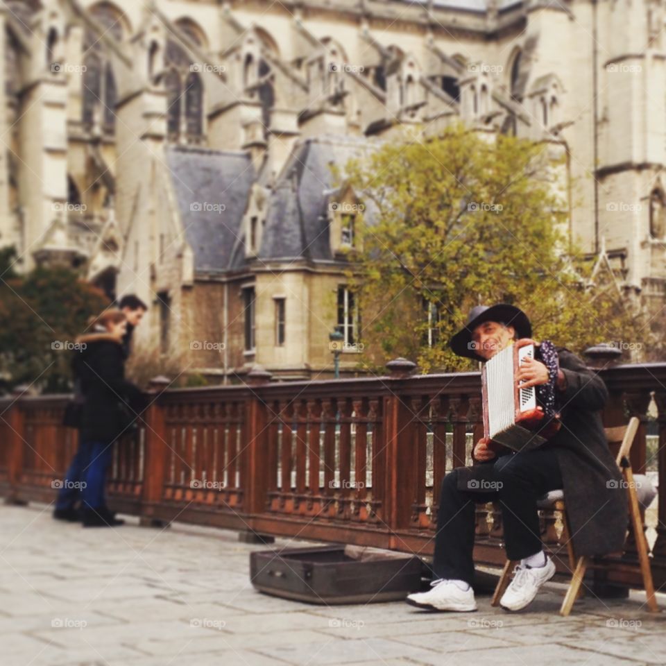 Notre Dame Street Performer. A man plays the accordion outside the Notre Dame Cathedral in Paris. A couple stops to enjoy the music in the background