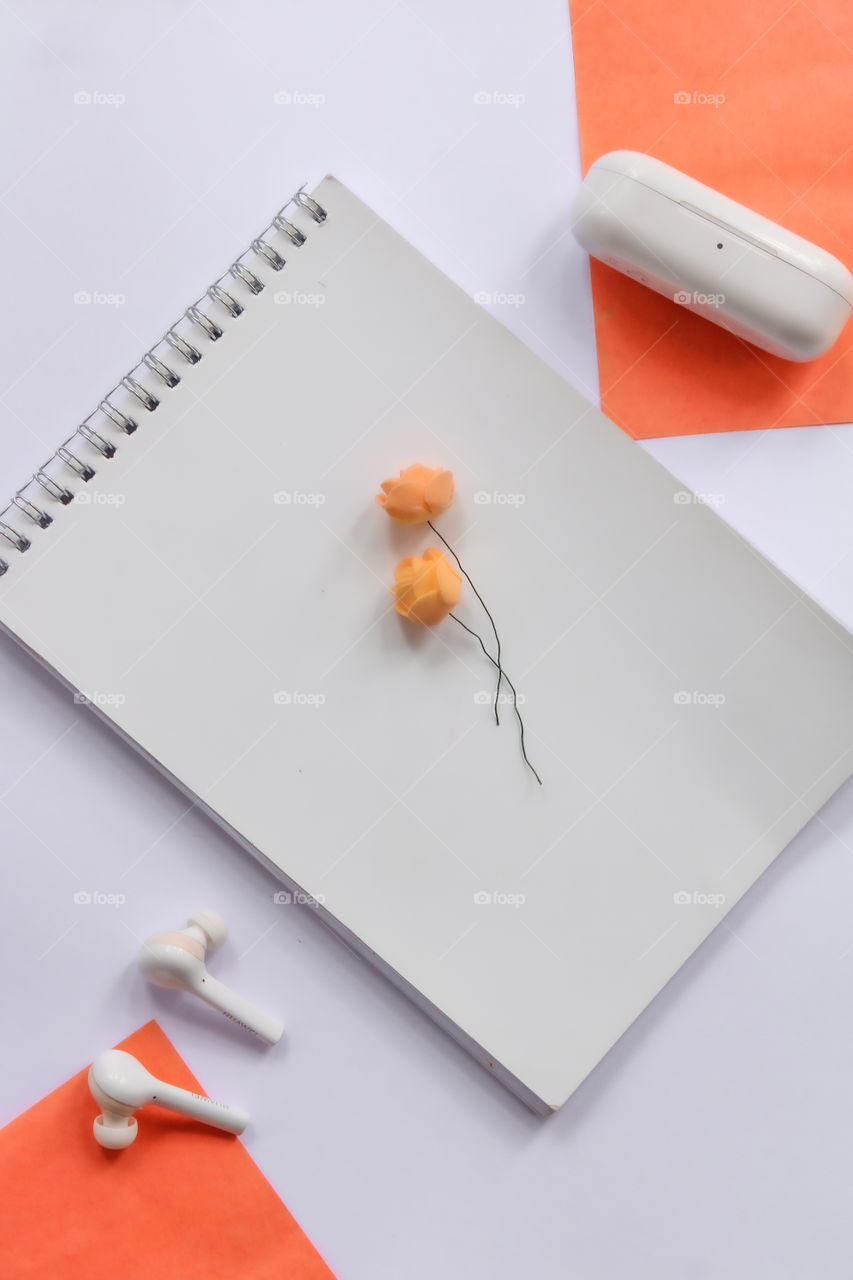 Book, flower and earphones on white and orange colour background. Take a break, rest with music and books.