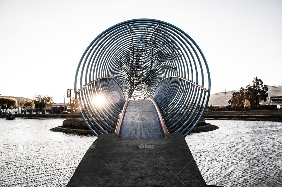 A bridge made of circular spiral shapes in a small lake in a park