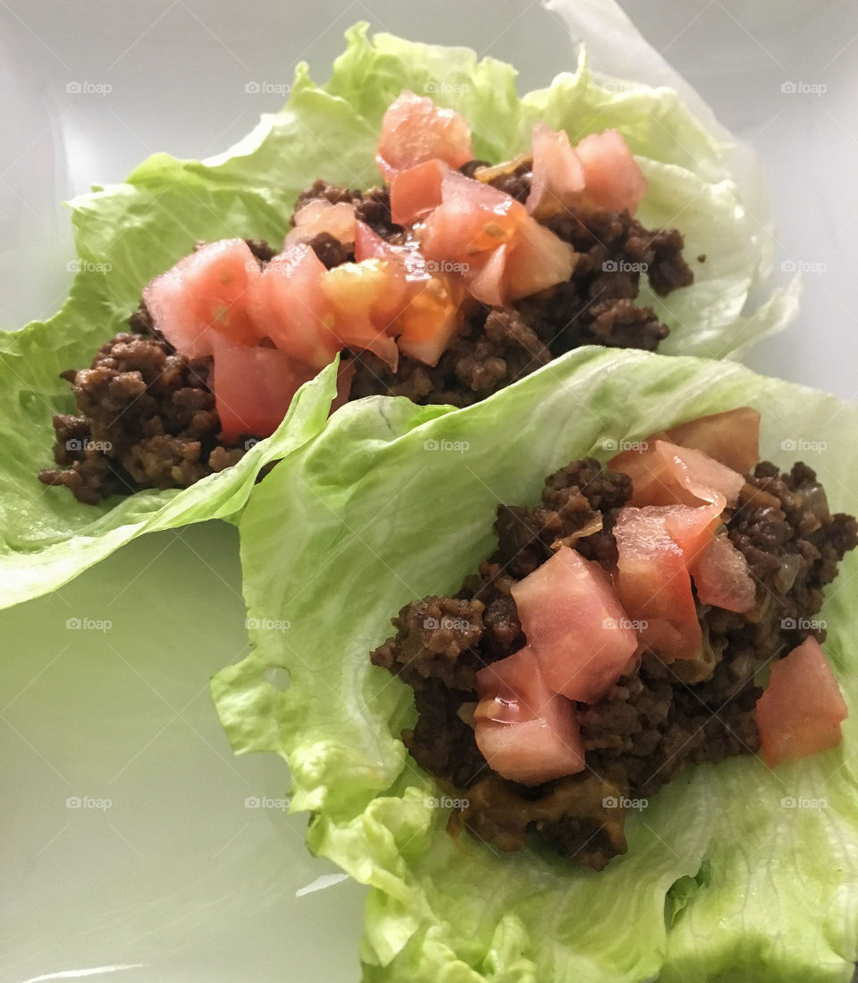 Paleo tacos featuring iceberg lettuce as the shell, ground beef and diced tomato.