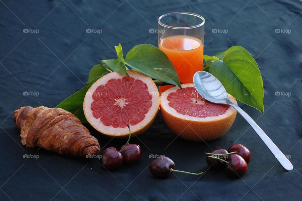 Healthy breakfast with fruit and juice , diet , croissant, orange juice, cherries , green leaves, grapefruit , spoon