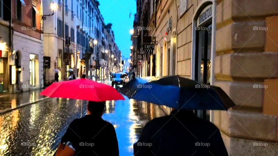 romantic couple walking side by side with umbrellas in the rain on an Italian cobble street with lights reflecting in the evening rain