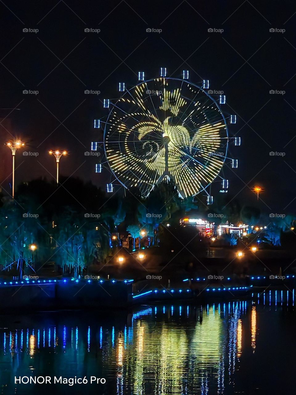 This photo captures the beautiful patterns created by lights on a Ferris wheel along the riverbank, as night falls and city lights illuminate the colorful surroundings. It showcases a stunning display of vibrant colors.It was taken in China and is in