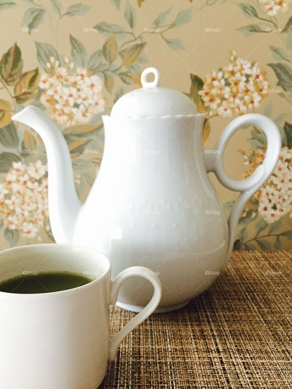 Tea Time - white porcelain teapot with white cup on bamboo surface, floral wallpaper background 