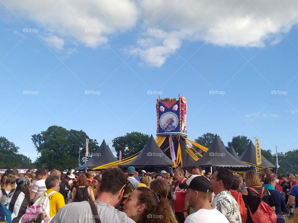 People pass each other in the crowd at a festival. In the foreground, a couple in love seems to be alone in the world despite the crowd.