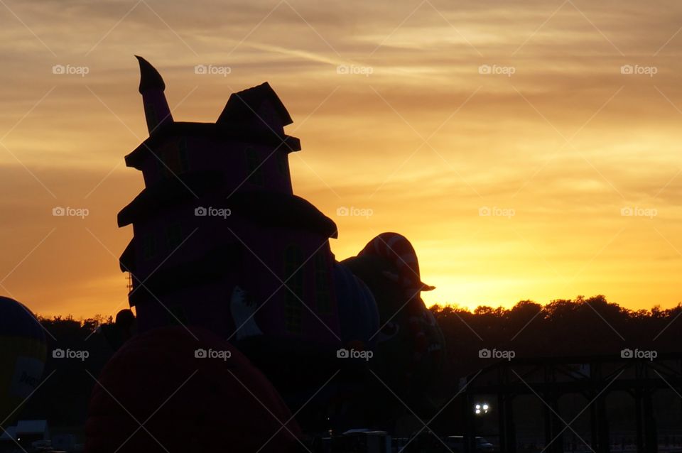 Setting sun sets sky ablaze behind haunted house balloon Silhouette.