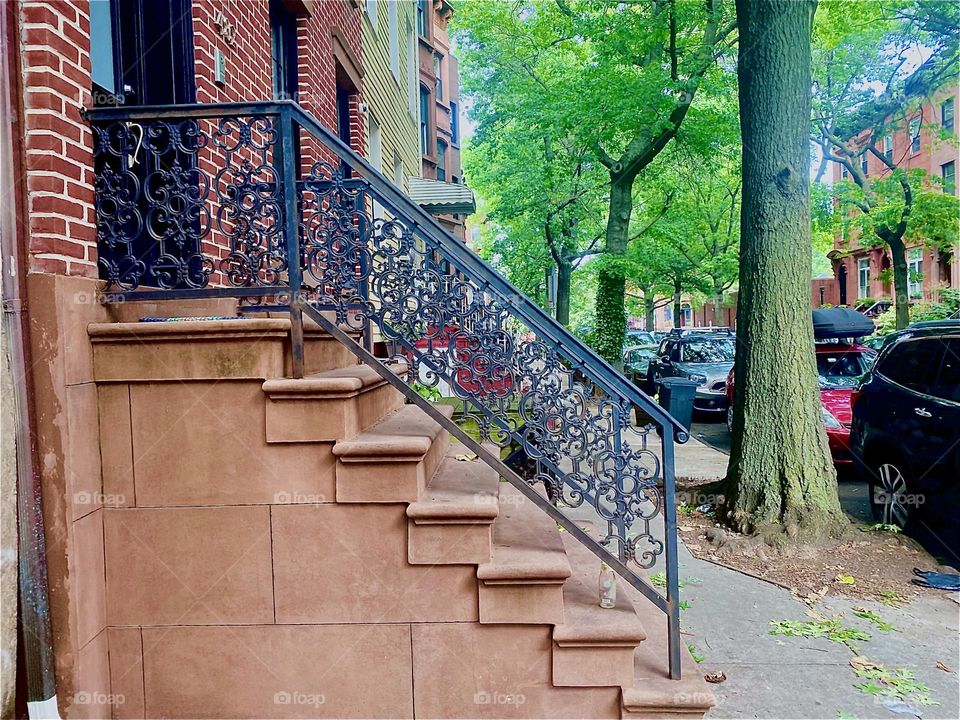A traditional „Brooklyn“ brownstone with a stoop that leads to the first story up above the ground floor and an ornamented railing. Often the first floor is situated halfway down and has its own entrance. 2023. Hypnotic Productions