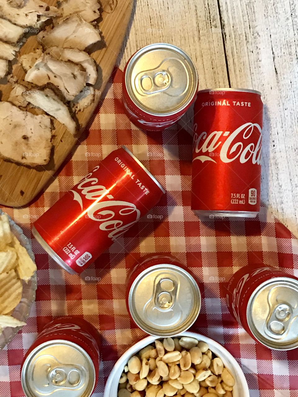 Cans of Coca-Cola on a red and white checkered background with barbecue food and potato chips 