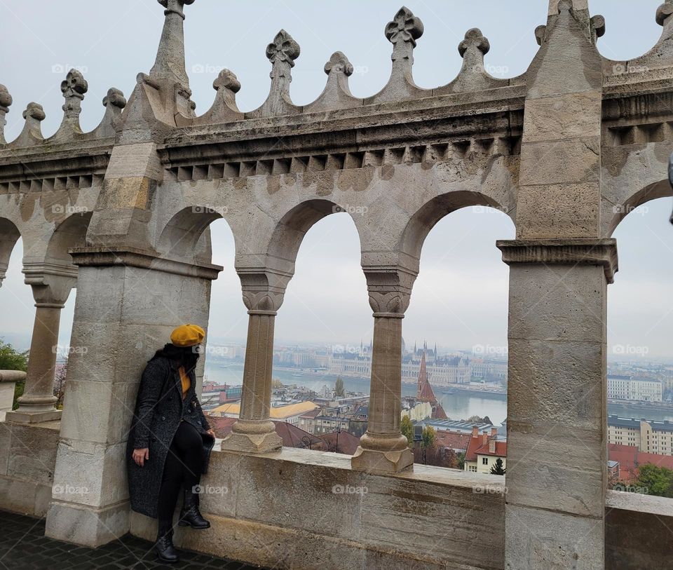 People in windows. A female sitting and looking through architectural windows in a historical wall, with the view of Budapest, Hungary.