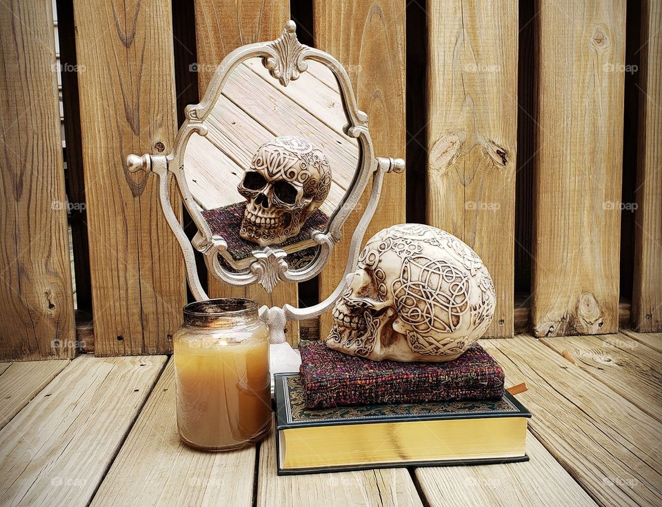 skull and candle sitting on a pile of books in frount of a mirror