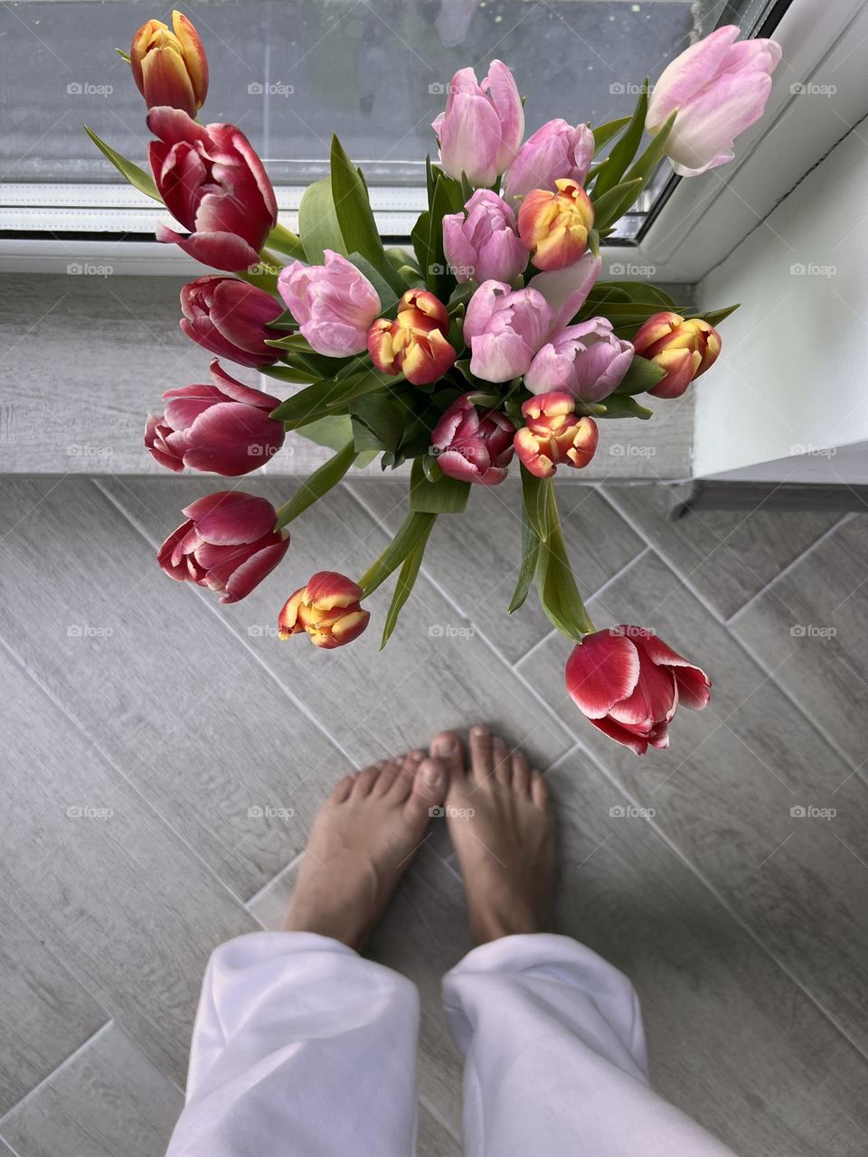 a bouquet of beautiful tulips stands in a vase on the window, the photo was taken from above, views of female legs