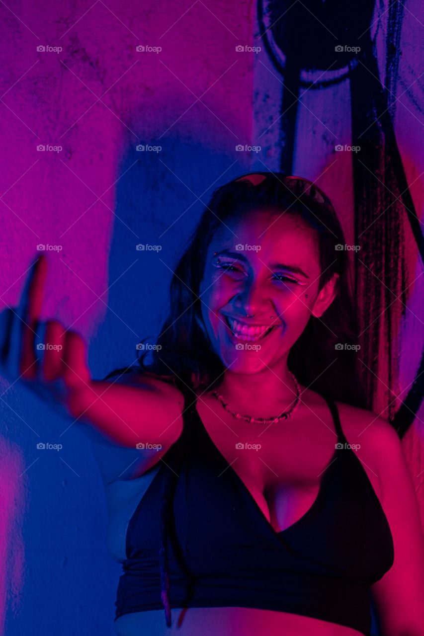 Retrato de garota mostrando o dedo do meio iluminada sobre luzes azuis e vermelhas.