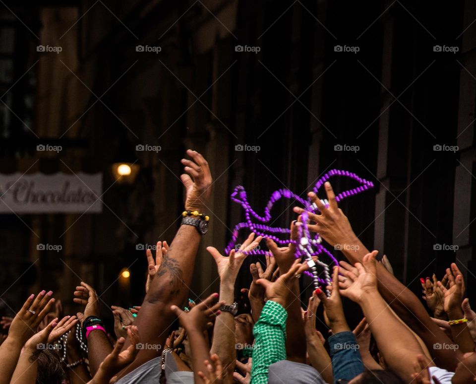 Crowd of reaching hands excitedly grasping at Mardi Gras beads thrown from a float in New Orleans, USA