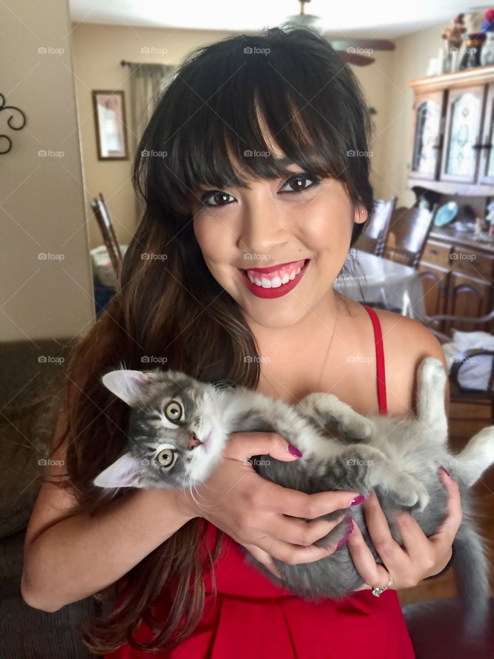 Pretty young woman in red dress and red lipstick holding a cute gray tabby kitten