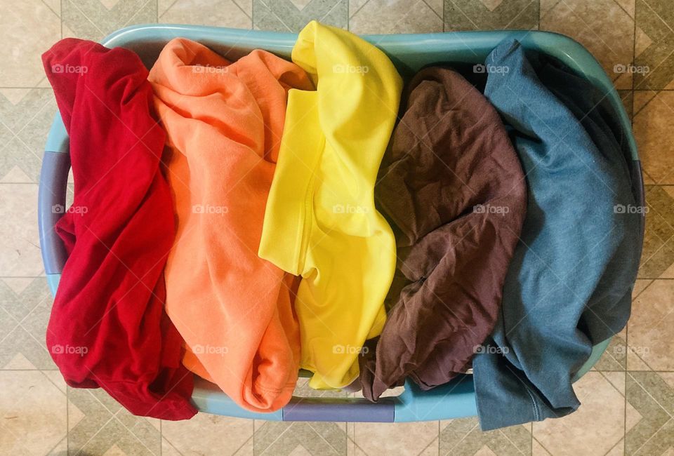The laundry basket is brimming over with clothes that display the beautiful colors of fall. 