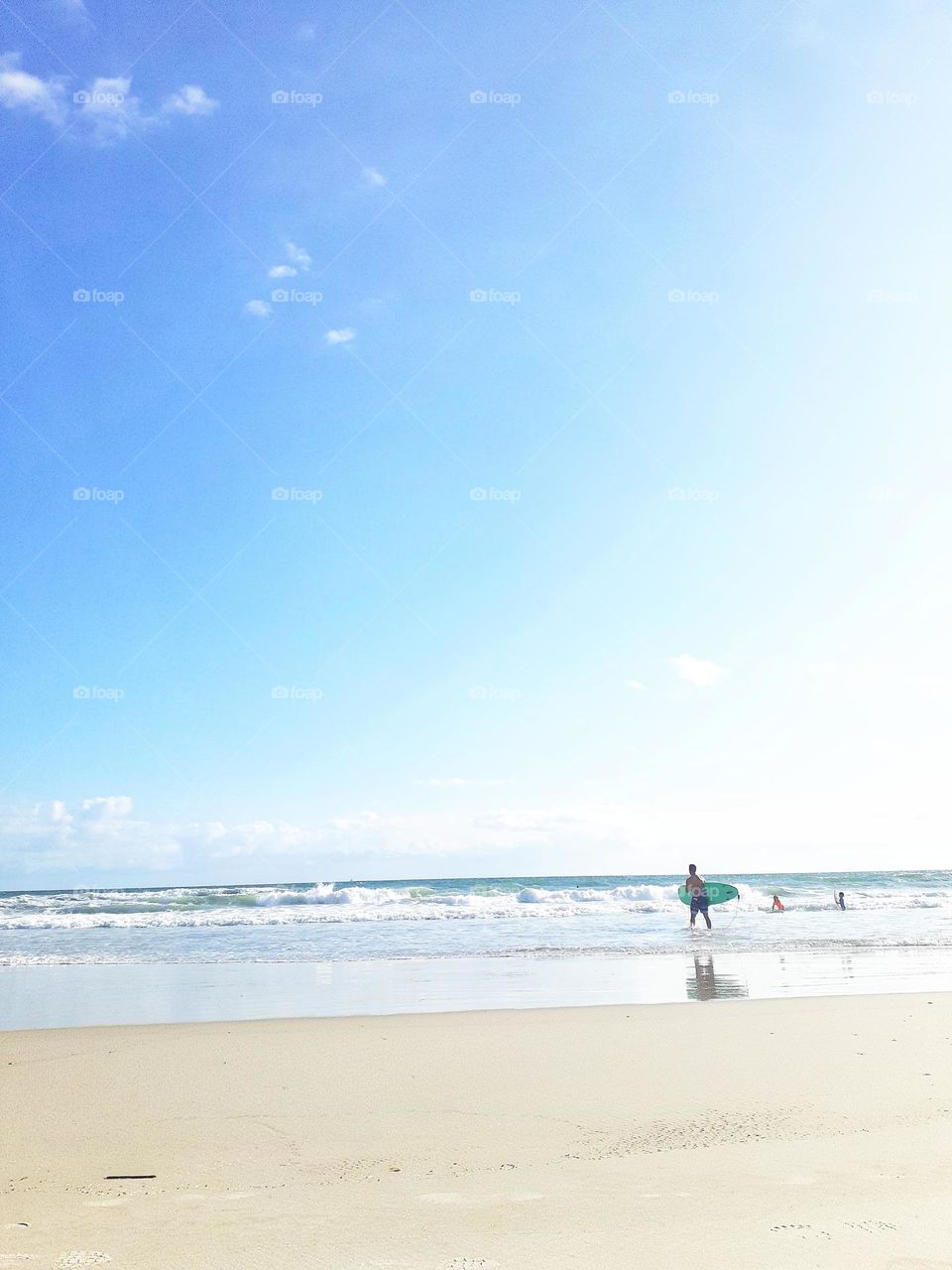 A surfer Carrie's his surfboard and walks into the ocean for a day of surfing at Ponce Inlet Beach in Ponce Inlet, Florida.