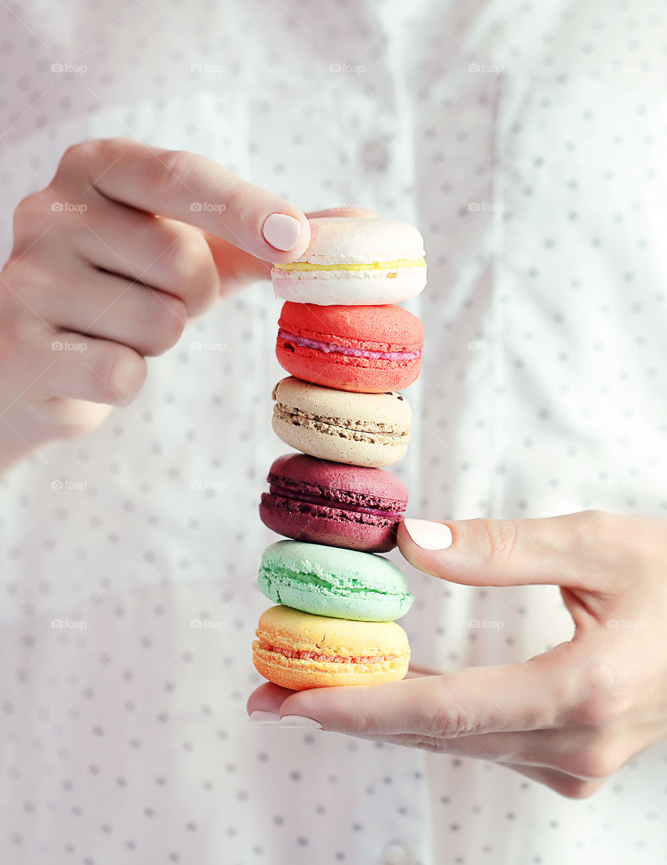 Tower of 5 colored macaron in the women hands on the background of the polka dots shirt