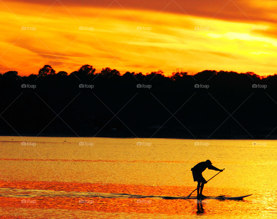 Silhouette of man paddle boarding in the lake at sunset