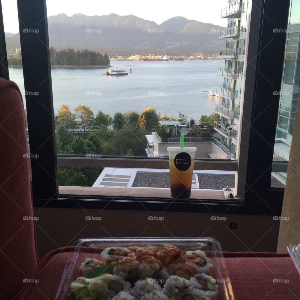 An order of sushi and bubble tea are placed in front of a window. Outside, a Vancouver harbour is visible.