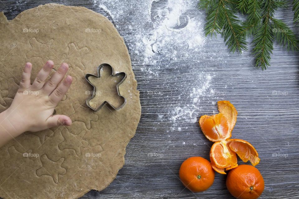 A small child helps to prepare festive, gingerbread cookies on a wooden table on Christmas Eve.