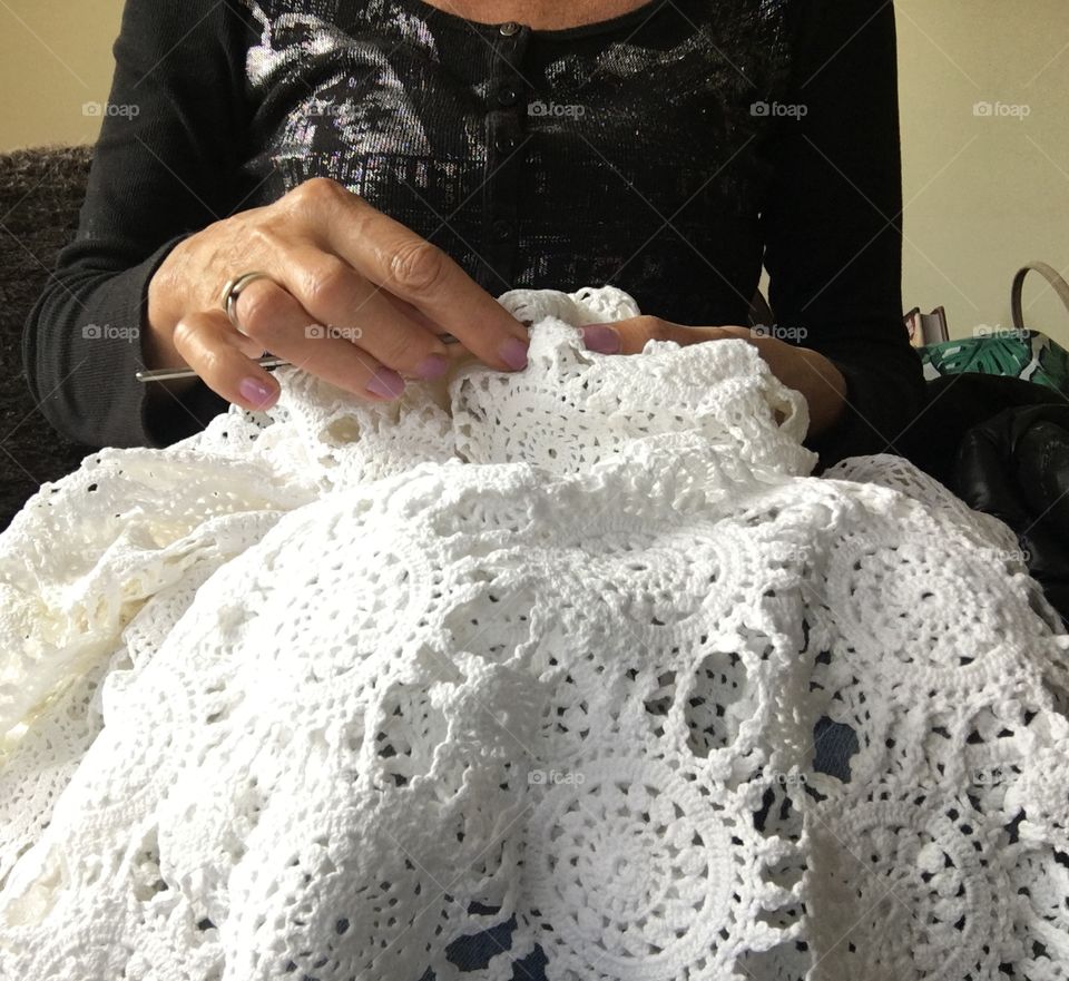 Woman crocheting lace table cloth cover using fine cotton thread and steel crochet hook, working women